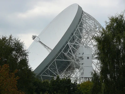 The gigantic Lovell radio telescope at Jodrell Bank Observatory, Lower Withington, England, United Kingdom, viewed through a gap in surrounding trees.
