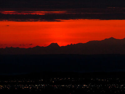 Very red sunset over the mountains outside Anchorage, Alaska, USA, with the lights of the city in the foreground.