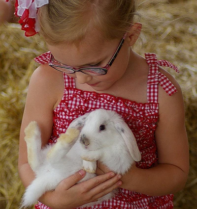 Young girl in a sundress and wearing glasses holding a white rabbit.