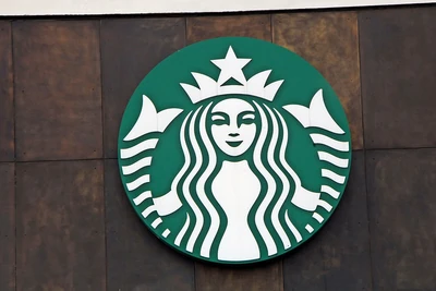 Green and white Starbucks 'siren' logo sign hanging on a brown wall.